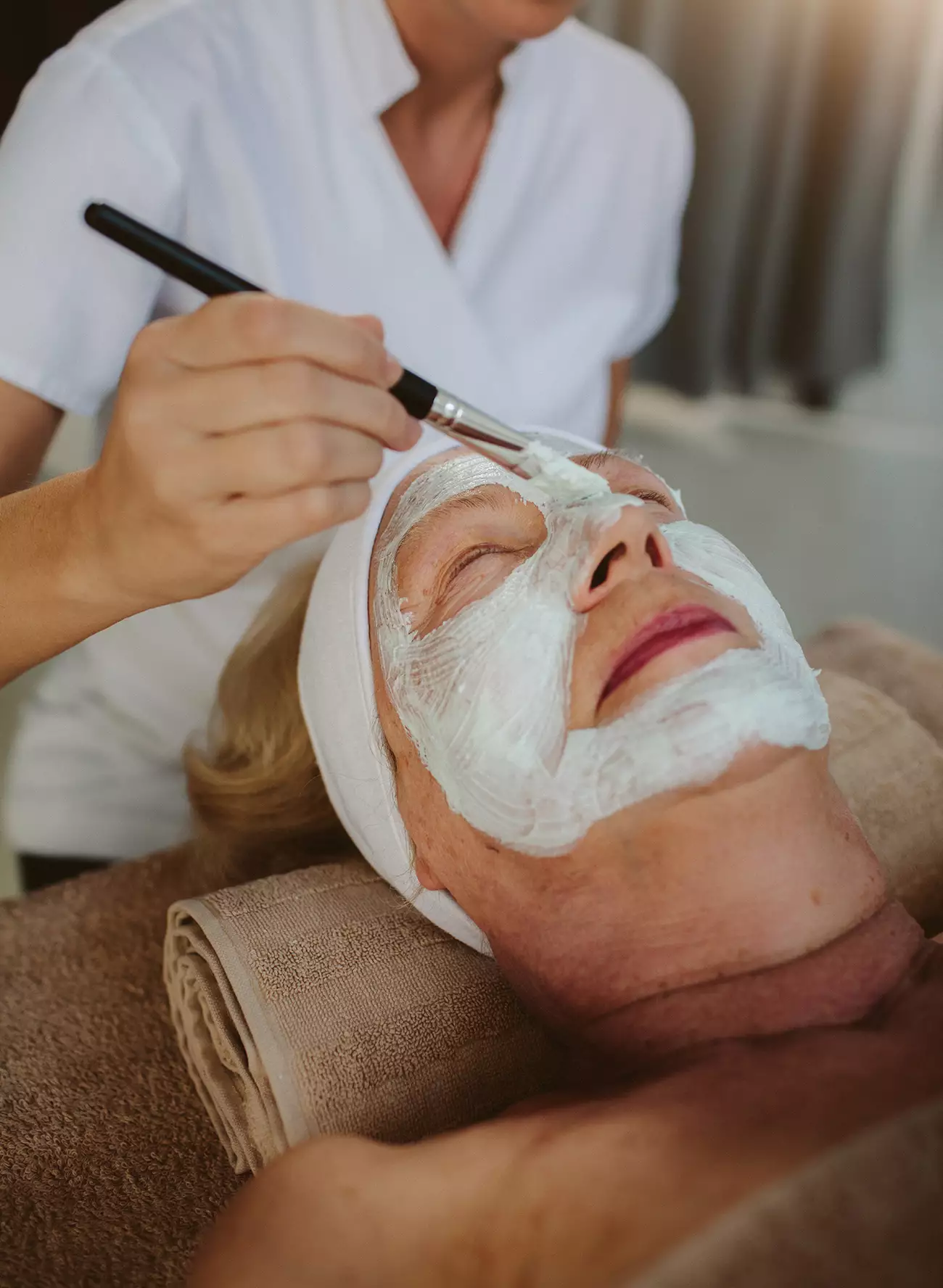 Mature woman enjoying a facial with skin care applied to face with brush